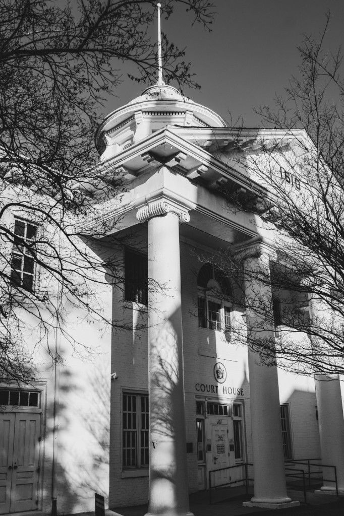 Monochrome photograph of a courthouse portico, dated 1810, framed by winter branches.