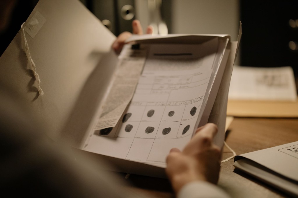 Hands holding an archival folder open to a fingerprint card — a physical record of identity and evidence.
