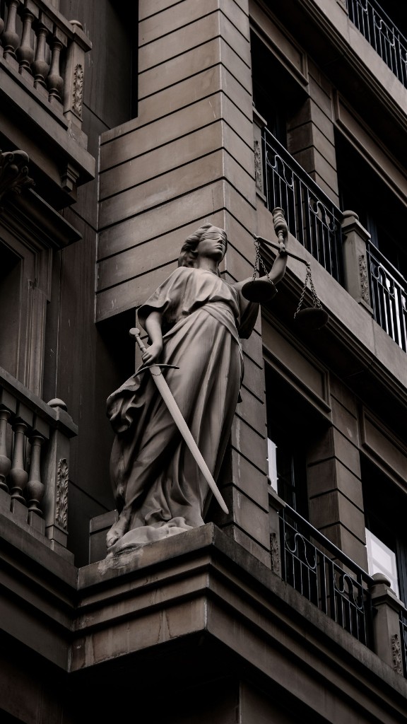 Stone statue of Justice, blindfolded, holding scales and a sword against a classical facade.